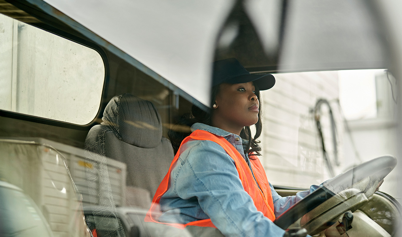 Woman with a bright orange vest sitting behind the steering wheel of a truck.