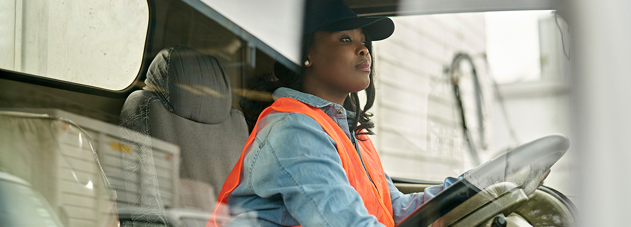 Woman with a bright orange vest sitting behind the steering wheel of a truck.